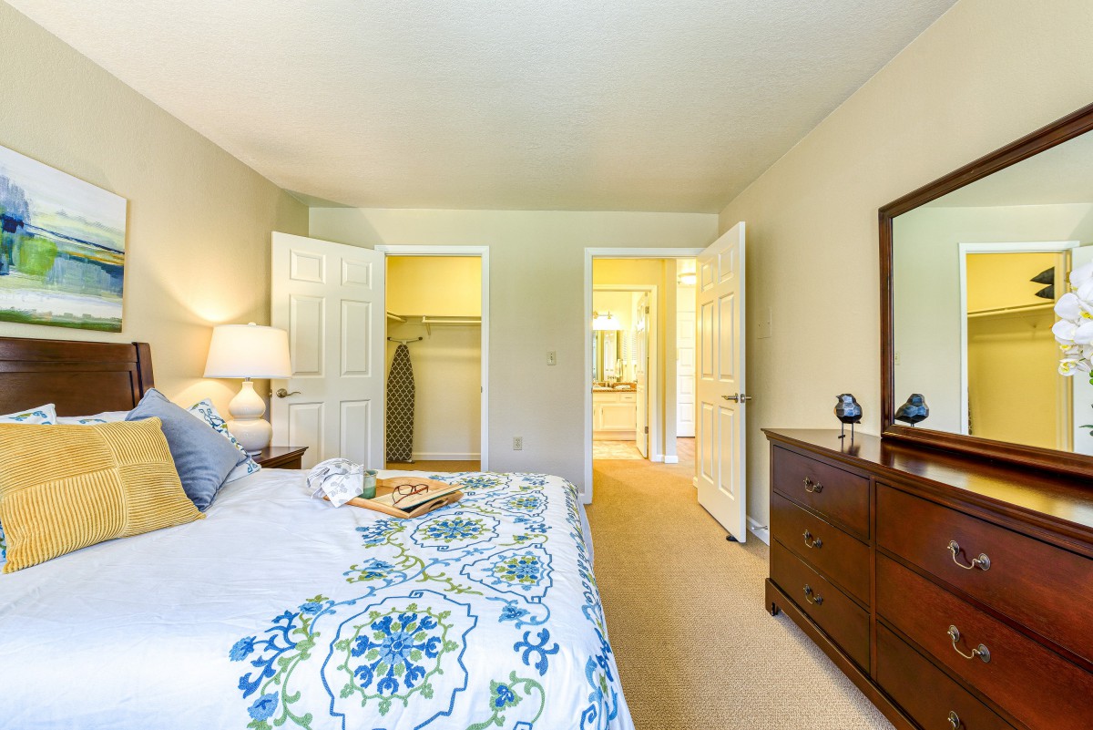 A cozy bedroom featuring a bed with patterned bedding, dresser with mirror, and an open closet.