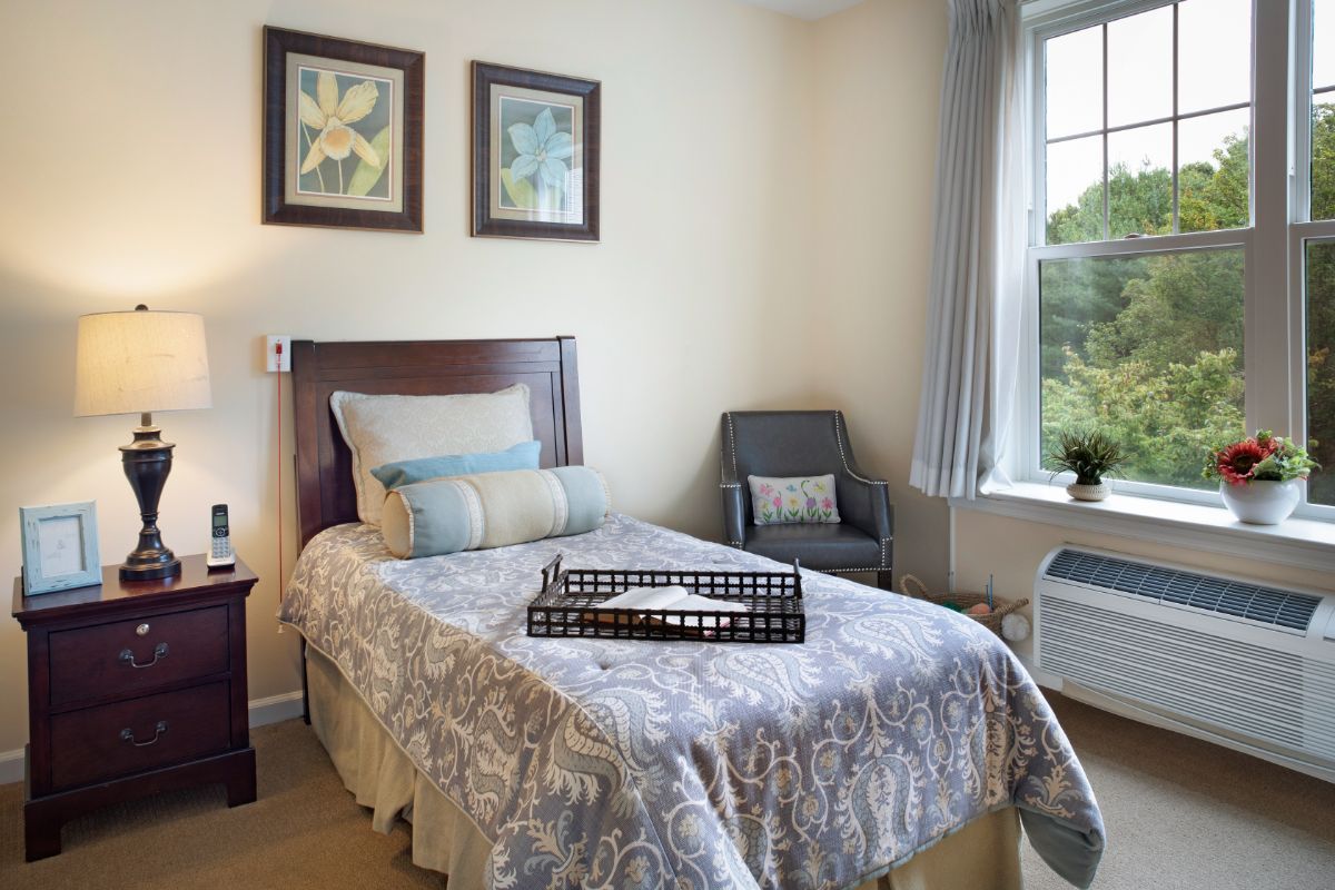 A cozy bedroom with a single bed, artwork on the walls, and a large window.