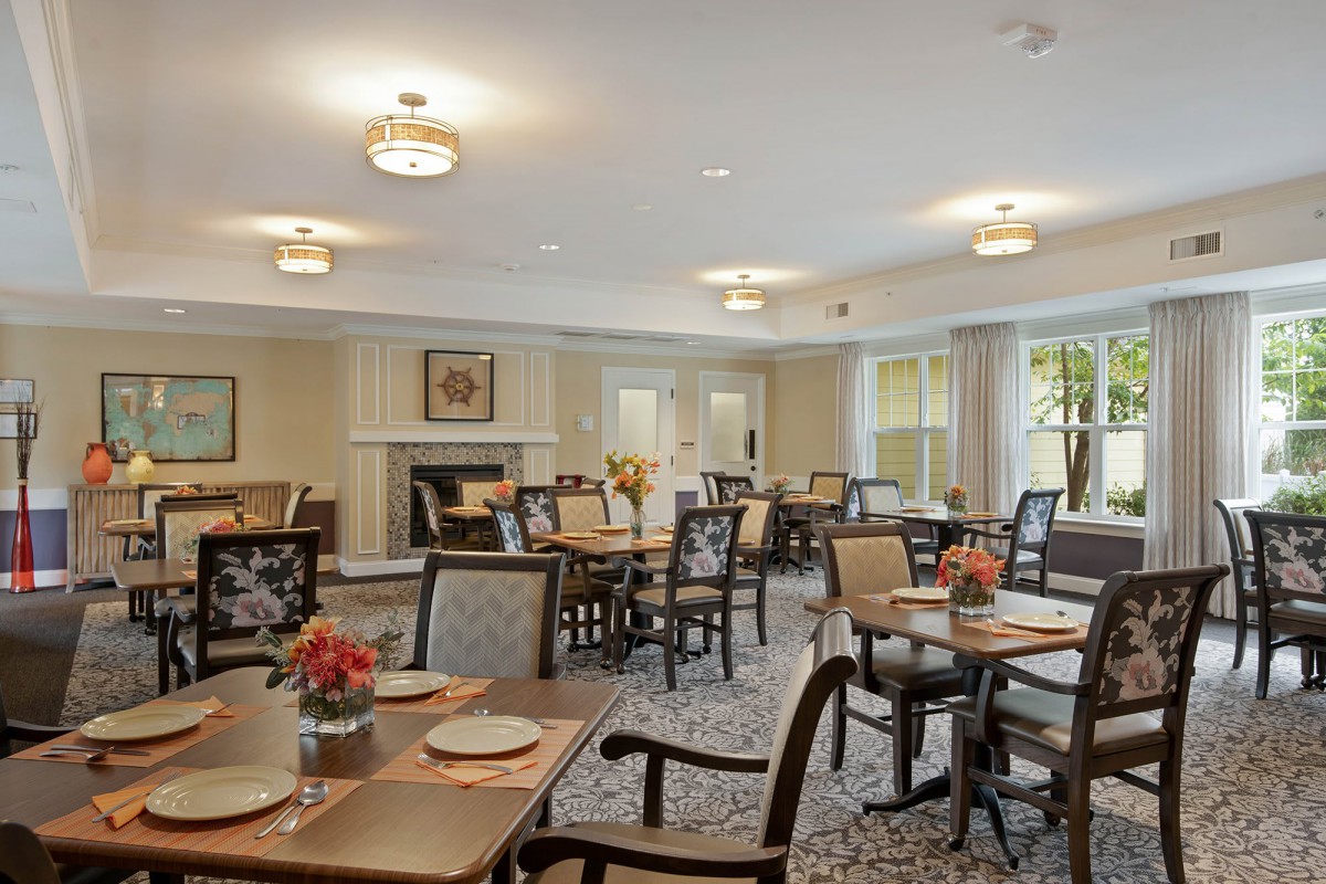 An elegant dining room with neatly arranged tables and chairs, featuring decorative flowers and warm lighting.