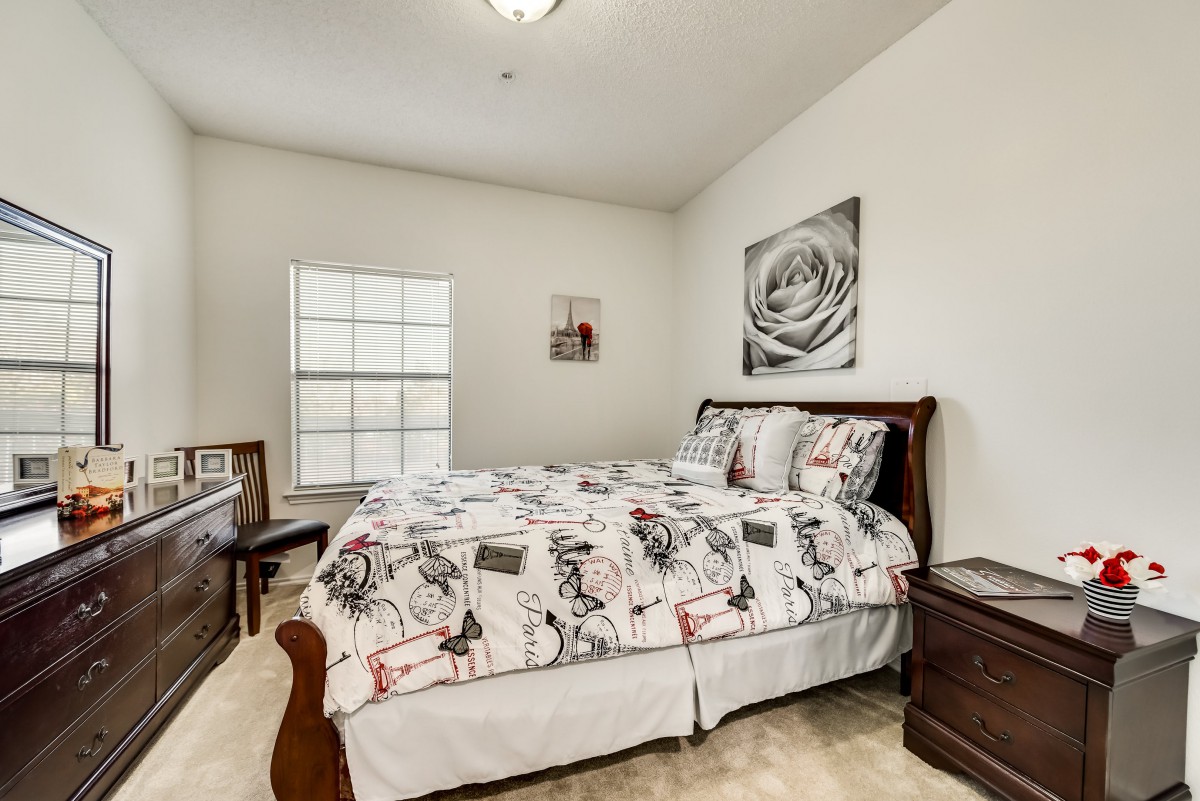 A cozy bedroom featuring a patterned bedspread, wooden furniture, and wall art.