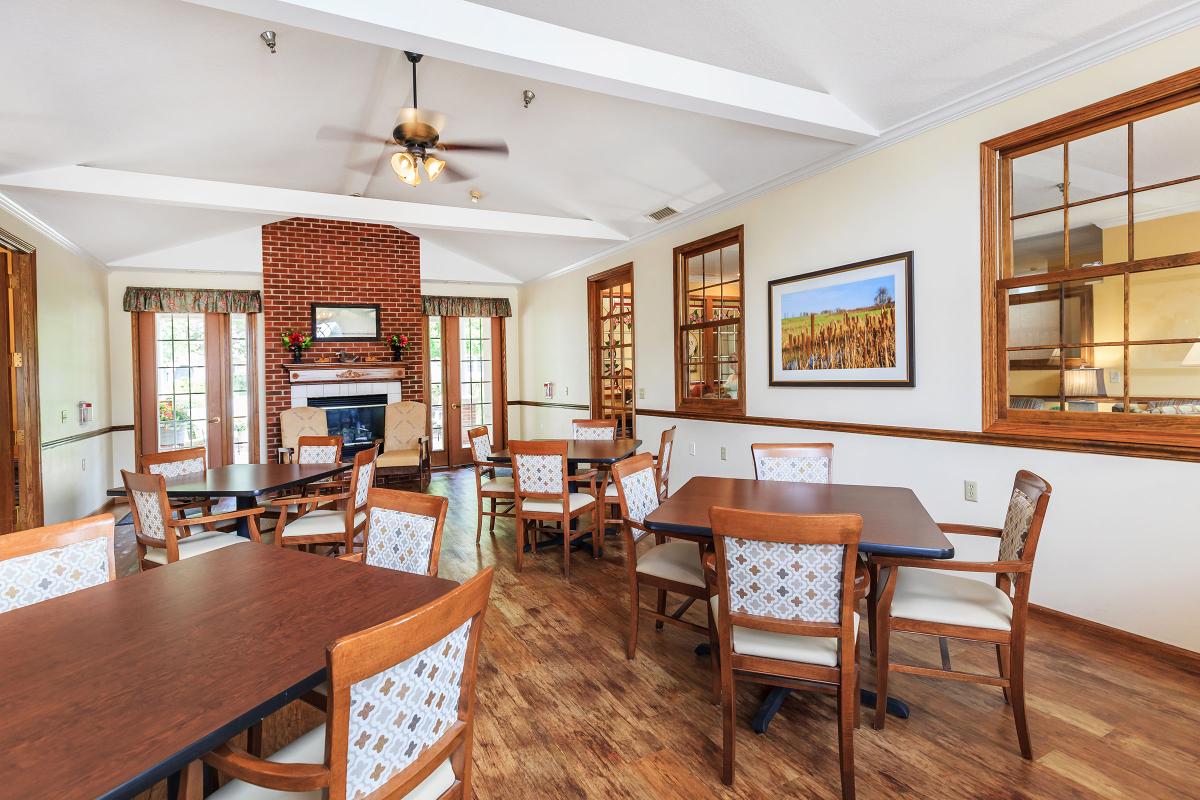 A cozy dining room with a brick fireplace, wooden floors, and neatly arranged tables and chairs.