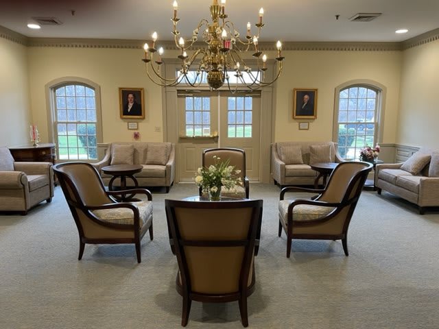 A well-appointed lounge with elegant furniture, featuring a chandelier and large windows.