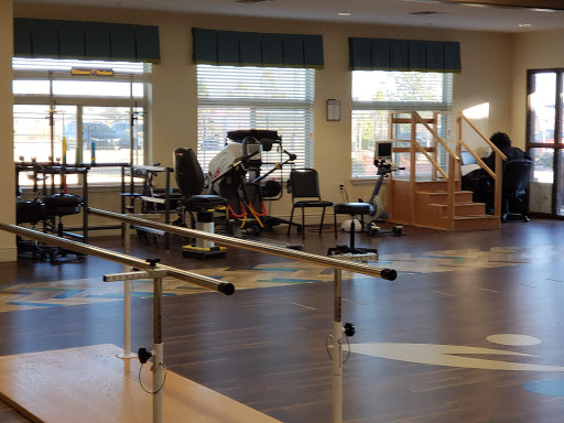 A spacious rehabilitation center equipped with various exercise machines and a barre for physical therapy.