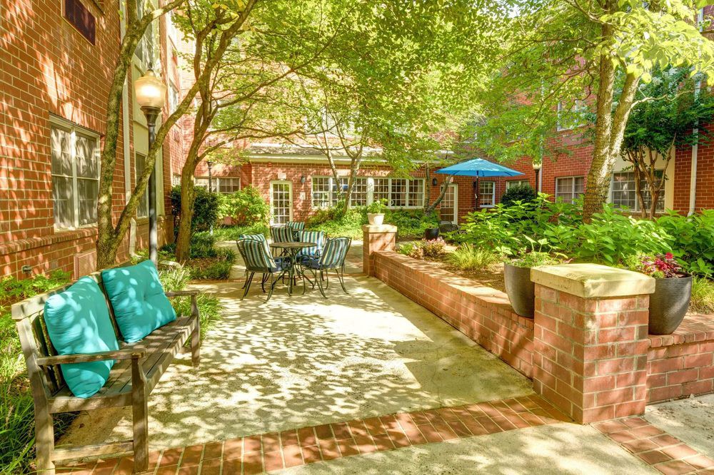 A sunny courtyard with comfortable outdoor seating, surrounded by lush greenery and brick buildings.