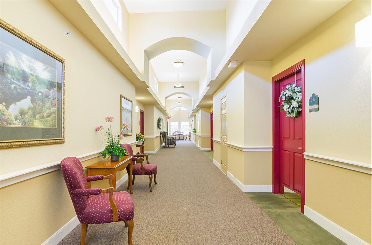 A brightly lit hallway with decorative elements, chairs, and a table lining the walls.