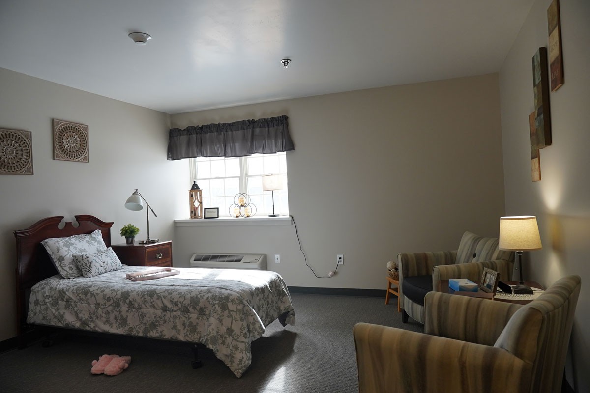 A cozy bedroom with a bed, lamp, and chairs near a window.