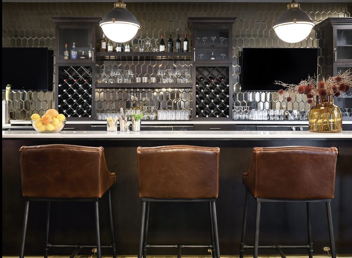 A modern bar setup with leather stools, well-arranged bottles, and elegant interior design.