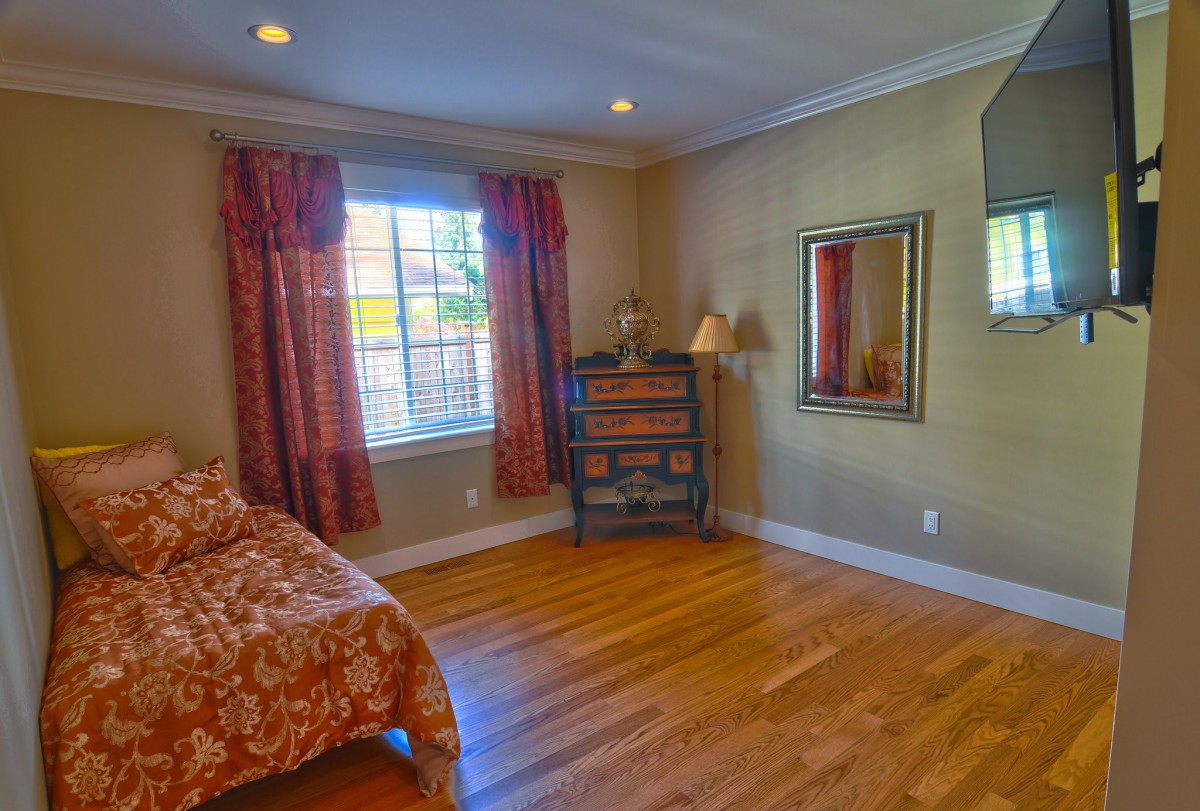 A cozy bedroom with a bed, window with curtains, and hardwood floors.