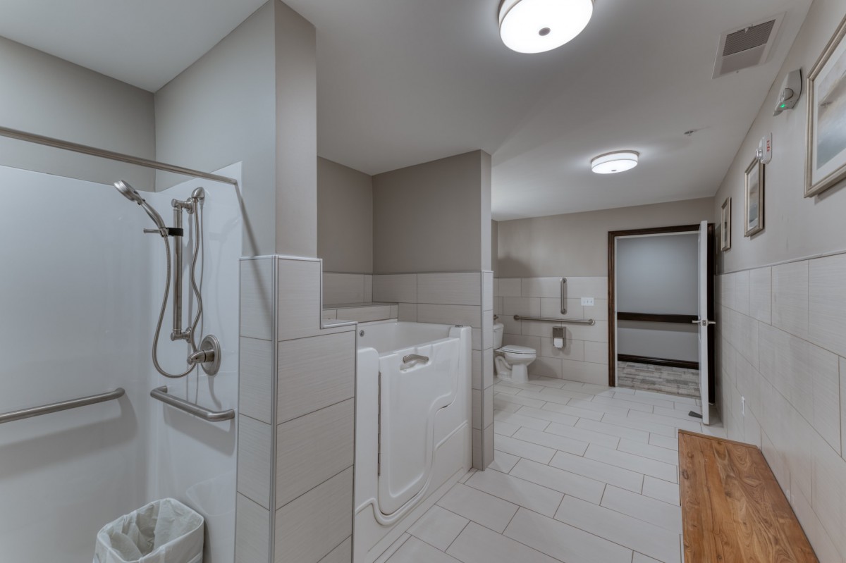 A spacious, accessible bathroom featuring a walk-in tub, shower, and safety grab bars.