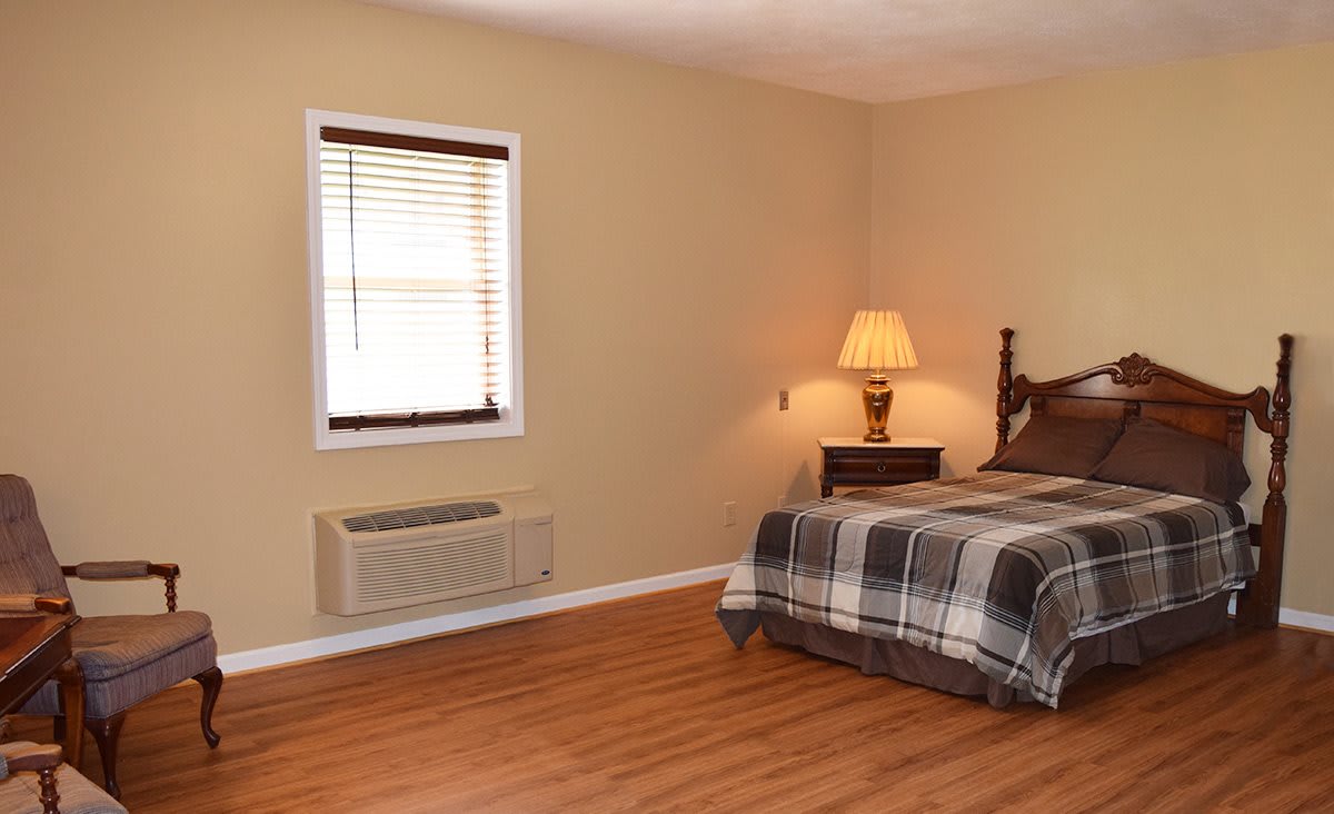 A cozy bedroom with a plaid bedspread, wooden floors, and a warm lamp.