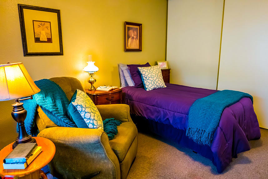 A cozy bedroom with a single bed, comfortable chair, and warm lighting.