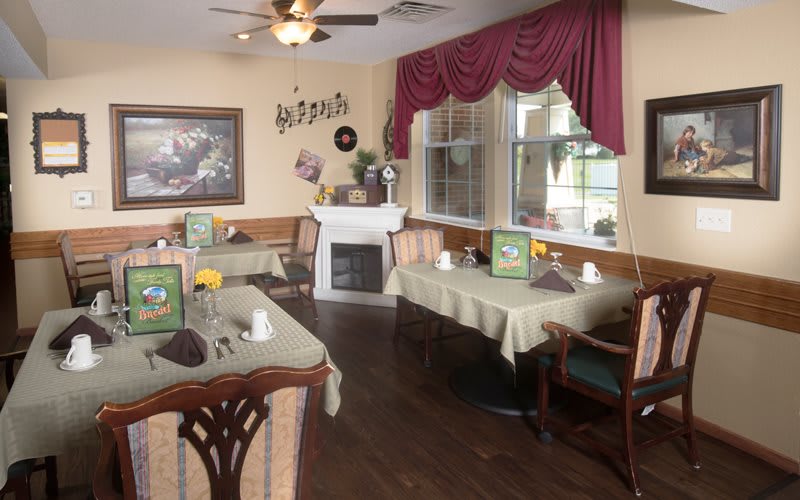 A cozy dining room with elegantly set tables, a fireplace, and decorative drapes.