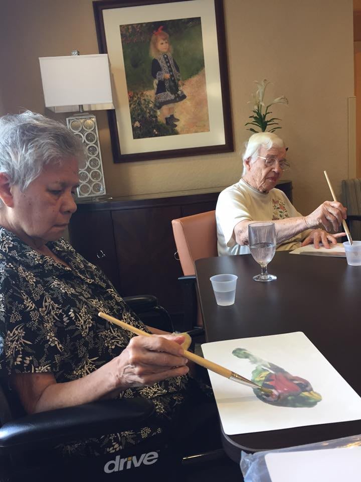 Two elderly individuals engaged in a painting activity during an art class.