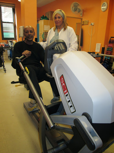 A person engaging in fitness activities on a rowing machine with assistance from a trainer.
