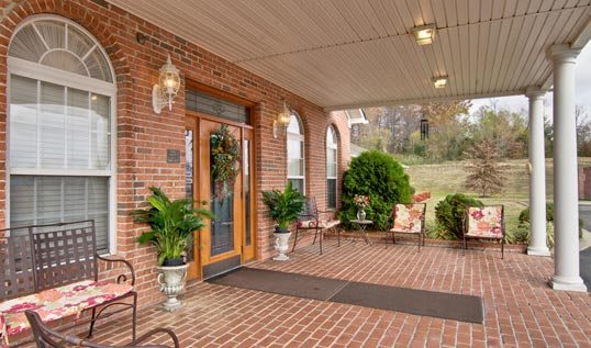 A welcoming porch entrance with brick walls, potted plants, and outdoor seating.