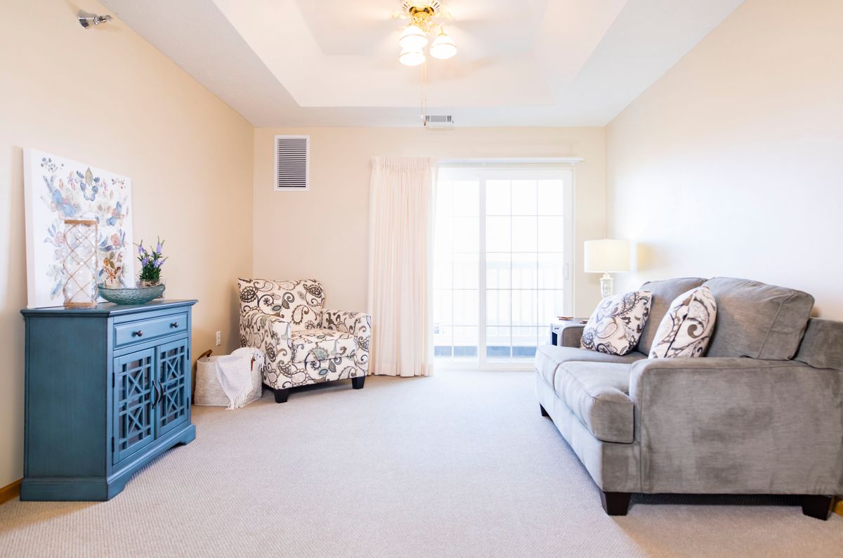 A bright and cozy living room with a couch, armchair, blue dresser, and decorative pillows.