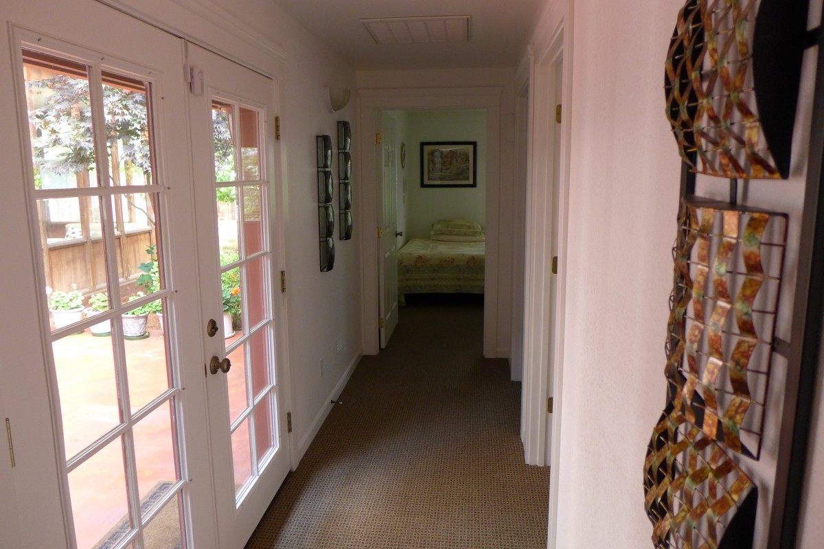 A narrow hallway with a view of a bedroom at the end, featuring glass doors leading outside.