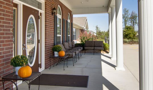 A welcoming front porch with comfortable seating and fall decorations, including pumpkins, at a brick house.