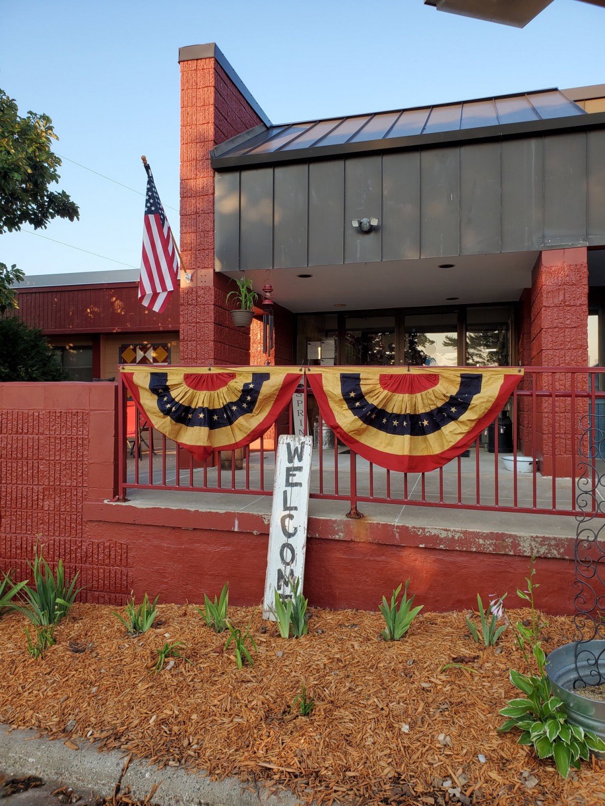 A building entrance decorated with patriotic bunting and a welcome sign, alongside an American flag.