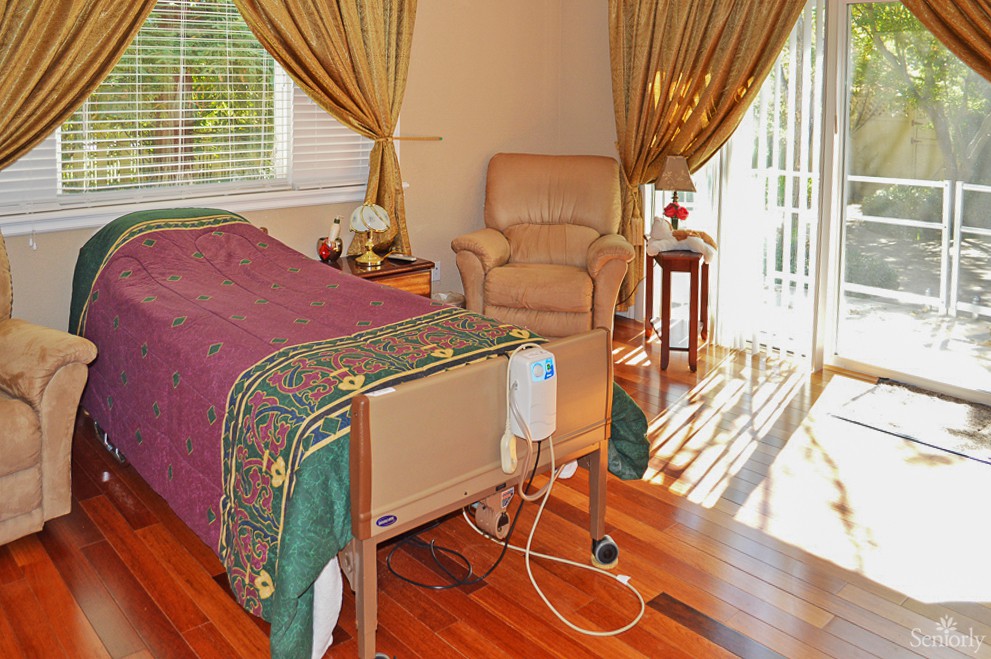 A cozy room with a hospital bed, armchair, and sunlight streaming through the curtains.