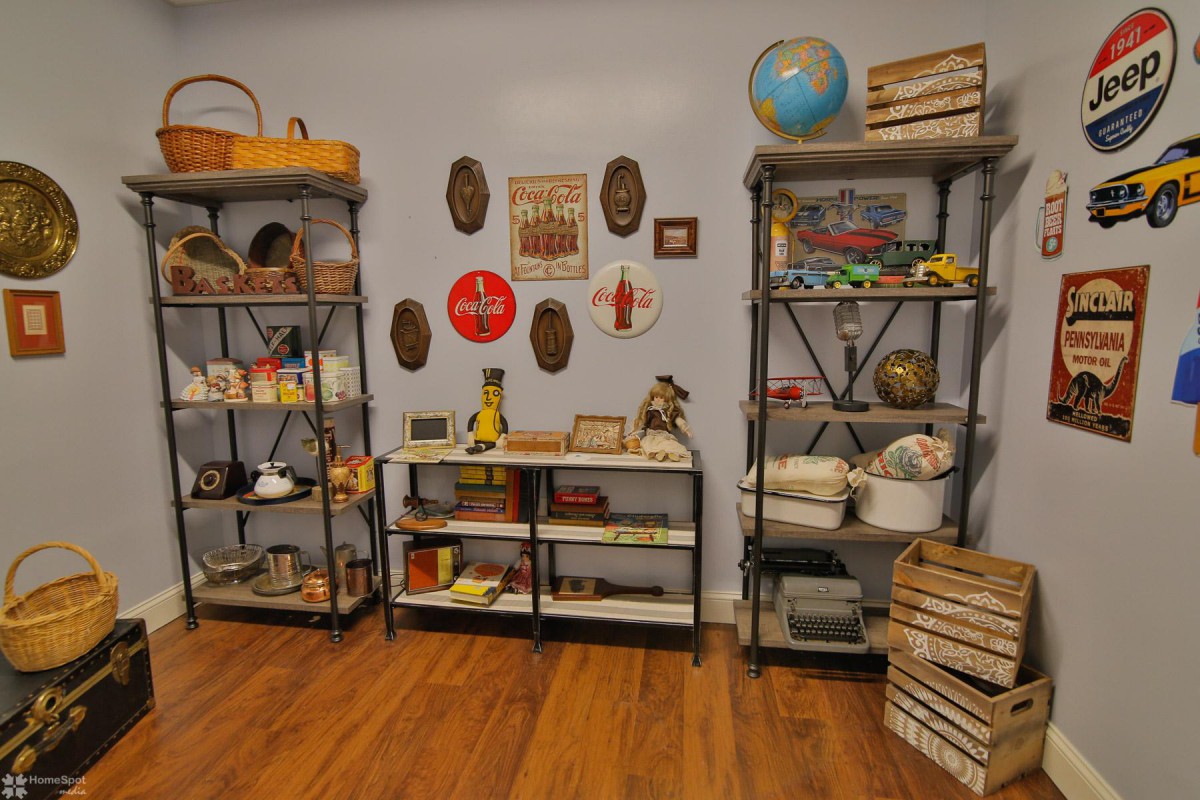 A room with vintage decor featuring shelves filled with books and various collectible items, including a globe and wall art.