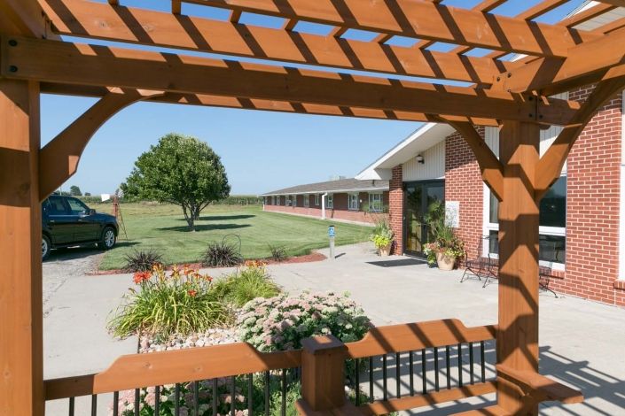 A building with a garden view framed by a pergola, featuring a tree on a sunny day.