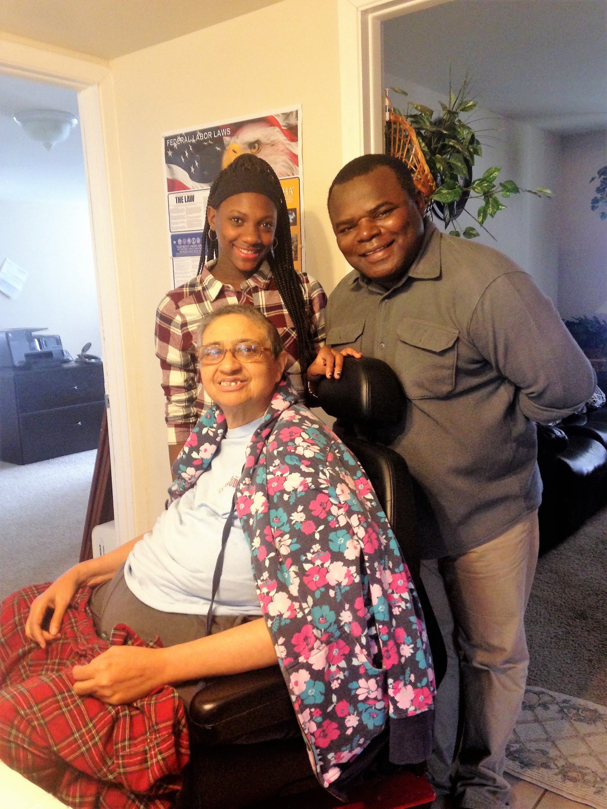 A happy family gathering indoors, with one person in a wheelchair and two others standing beside them.