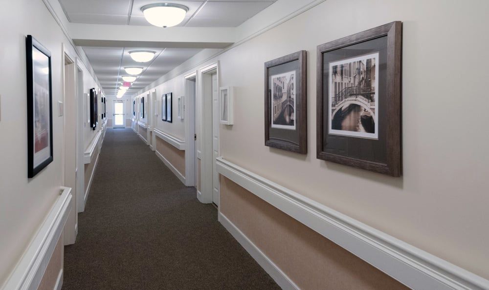 A long, carpeted hallway with framed pictures on the walls and overhead lighting.