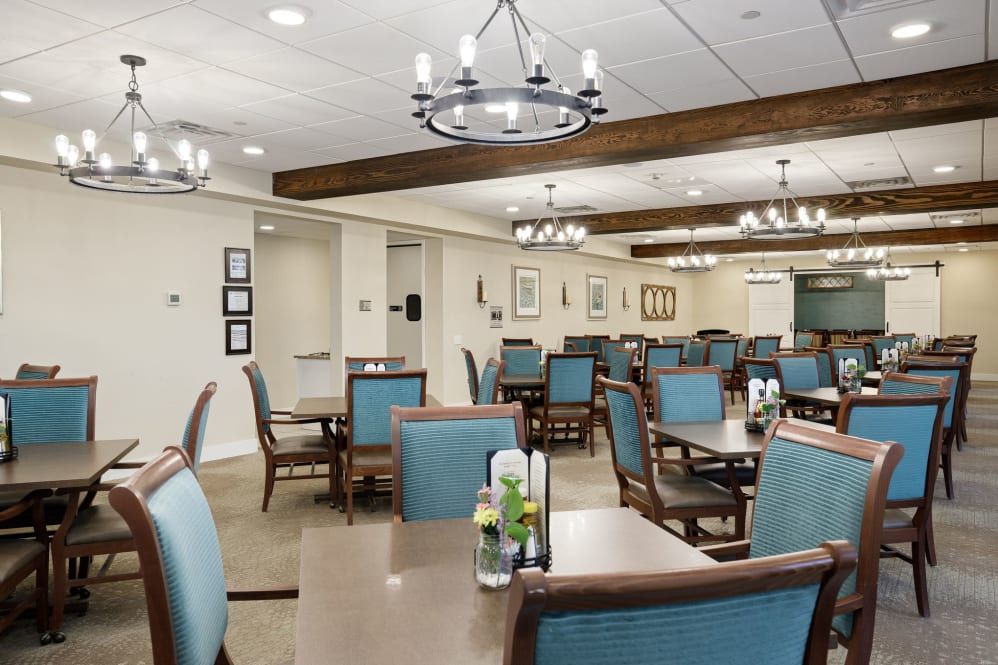 A modern dining area featuring elegant chandeliers and wooden beams, with neatly arranged tables and chairs.