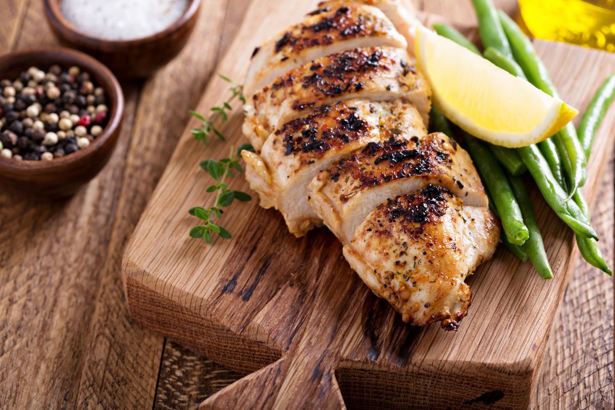 Grilled chicken breast served with lemon and green beans on a wooden board.
