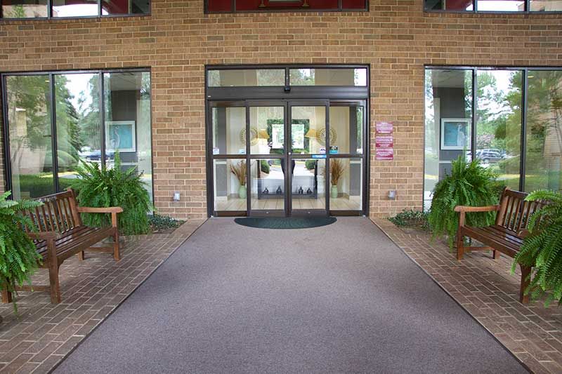 Entrance with glass doors and surrounding plants at a brick building.