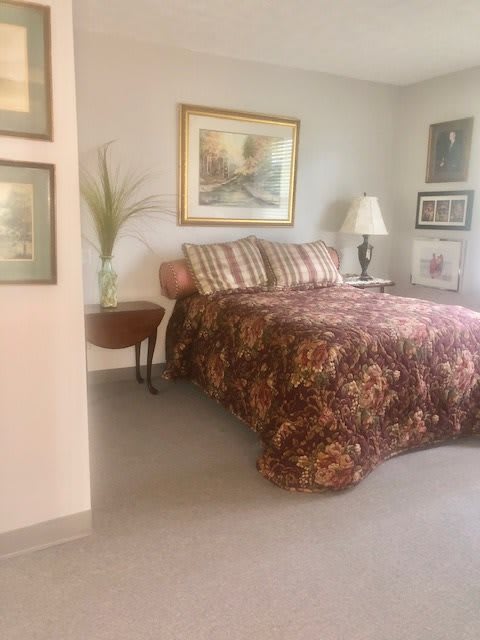A cozy bedroom with a patterned bedspread, artwork on the walls, and a side table with a lamp.