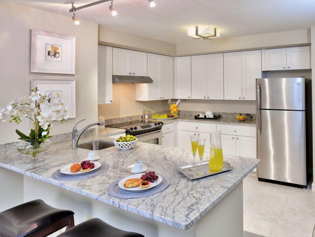 A modern kitchen with white cabinets, stainless steel appliances, and a granite countertop breakfast bar.
