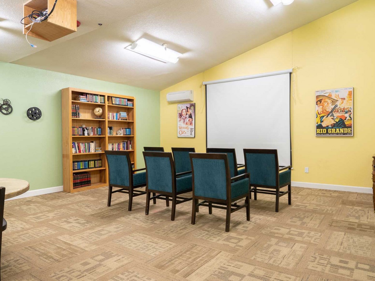 A small meeting room with chairs arranged in front of a projector screen and a bookshelf beside them.