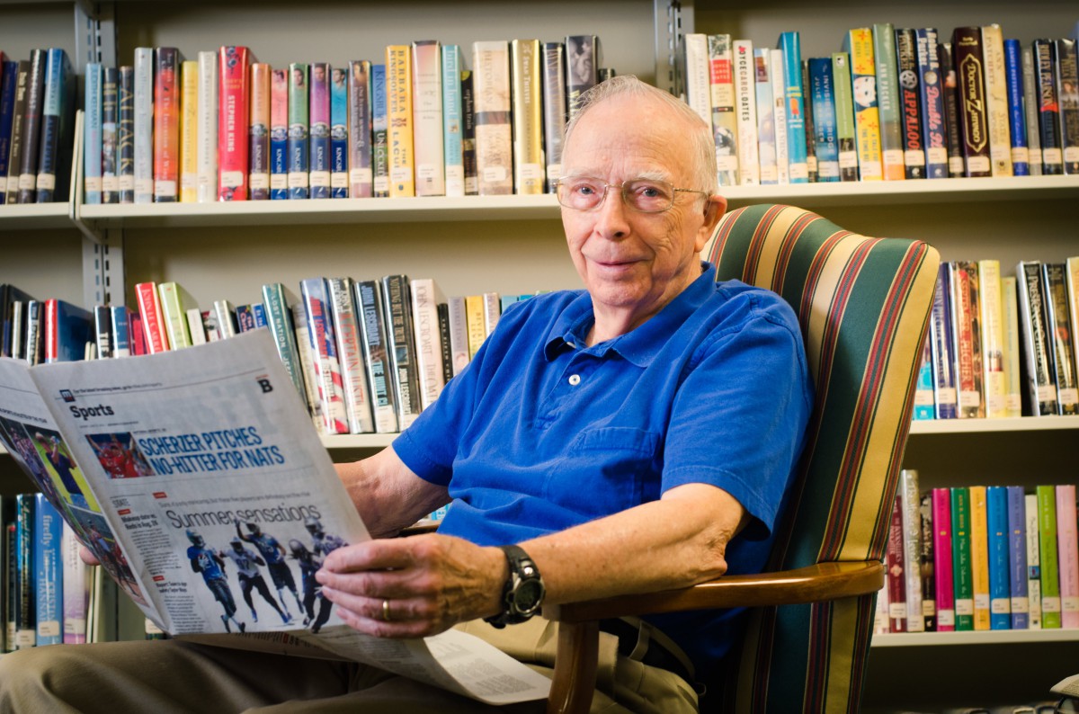 A man sitting in an armchair reading a publication in a library.