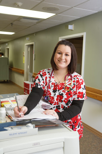 A nurse in colorful scrubs smiling while taking notes in a hospital setting.