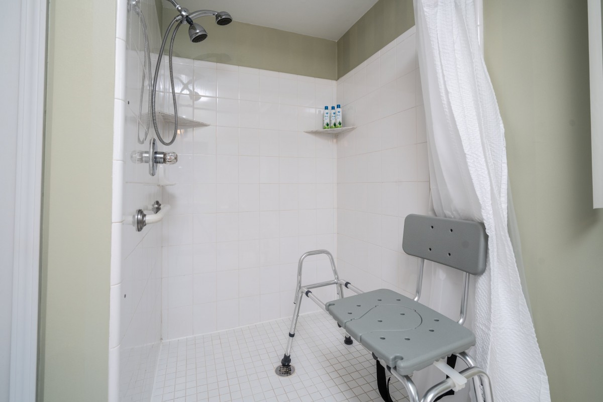An accessible shower with a safety chair and white curtain.