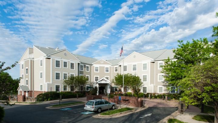 A hotel building with a parking lot and trees under a cloudy sky.