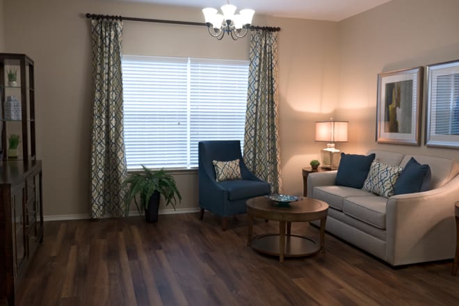 A cozy living room with a blue armchair, a sofa, and a round coffee table on hardwood flooring.