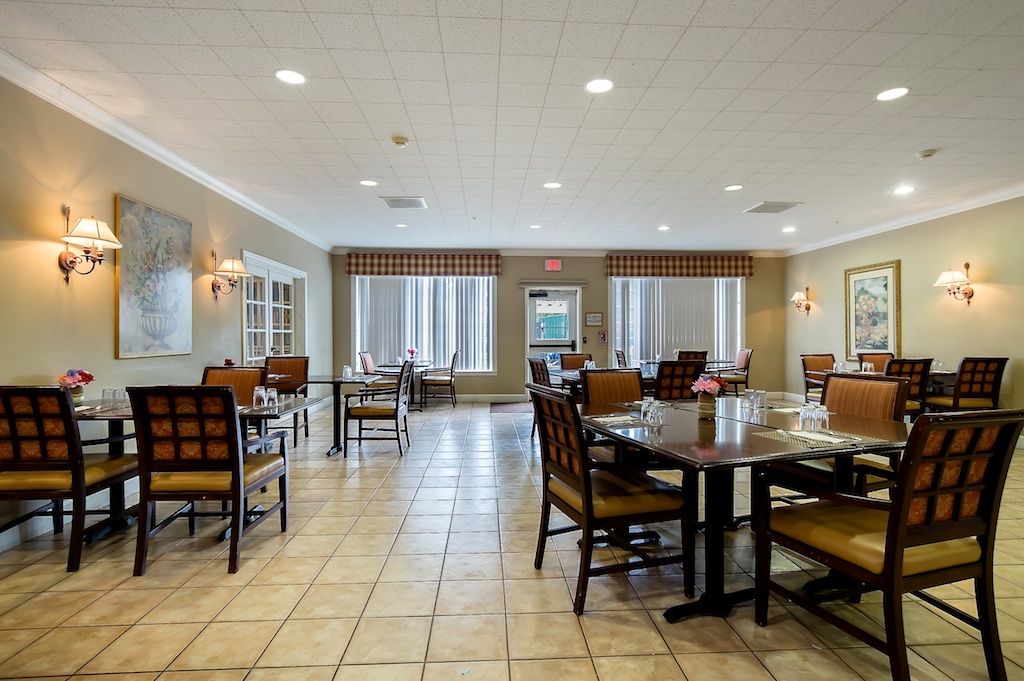 A spacious dining area with neatly arranged tables and chairs, illuminated by overhead lighting and natural light from the windows.
