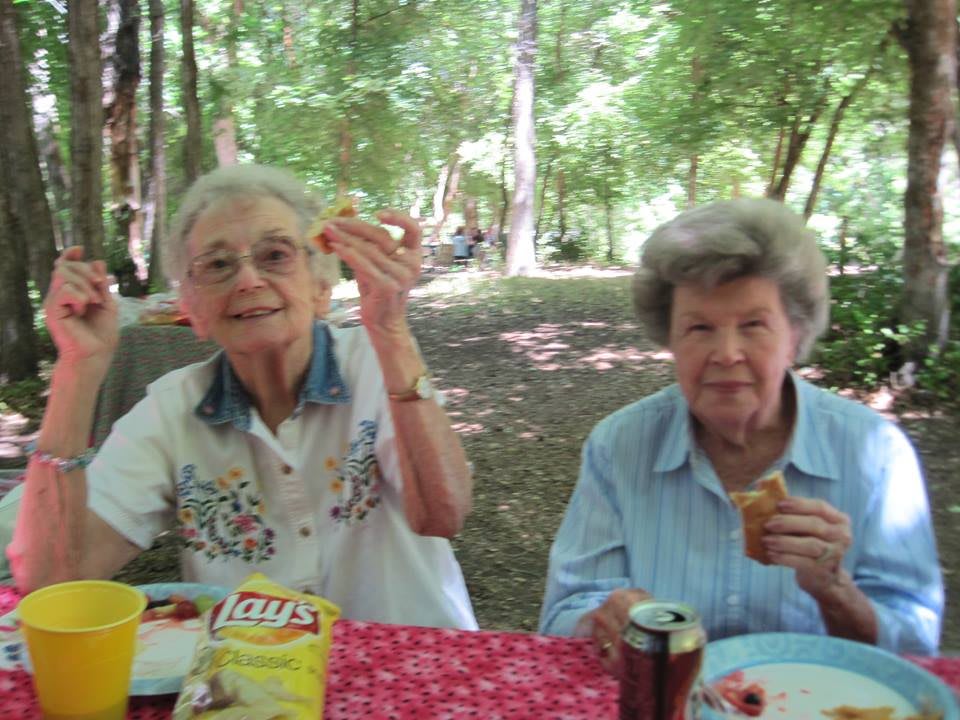 Two elderly women enjoying a picnic in a wooded area.