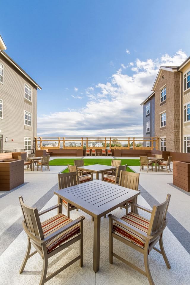 A spacious outdoor patio area surrounded by apartment buildings with tables and chairs, under a partly cloudy sky.