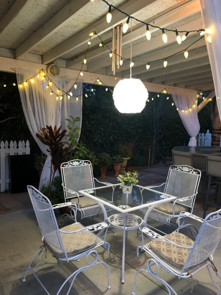 A cozy outdoor dining area with string lights and a glass table set for an evening gathering.