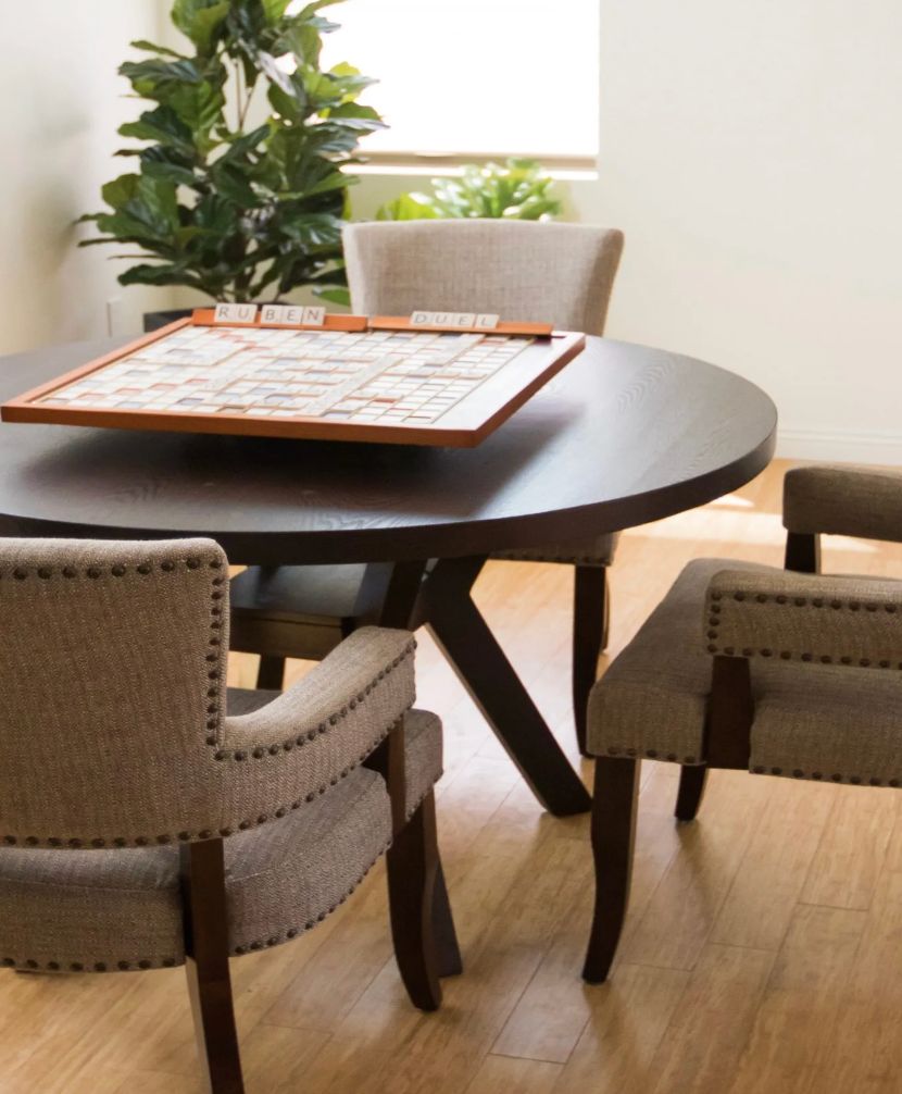 A round table with a game board is surrounded by upholstered chairs in a cozy indoor setting.