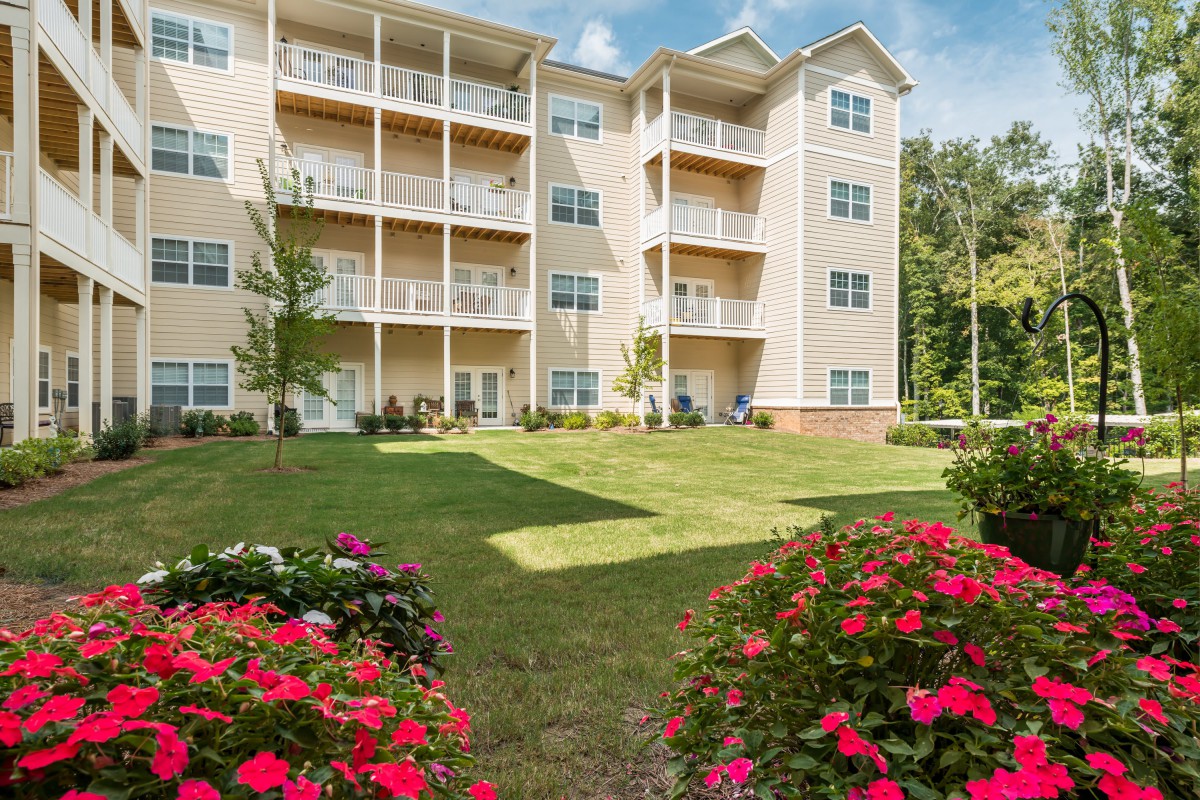 A modern apartment building with balconies, surrounded by a well-maintained garden with vibrant flowers.