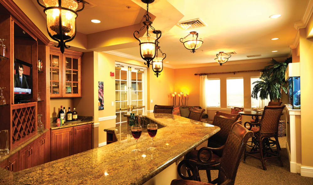 A cozy bar area with a granite counter, warm lighting, and wine glasses on display.