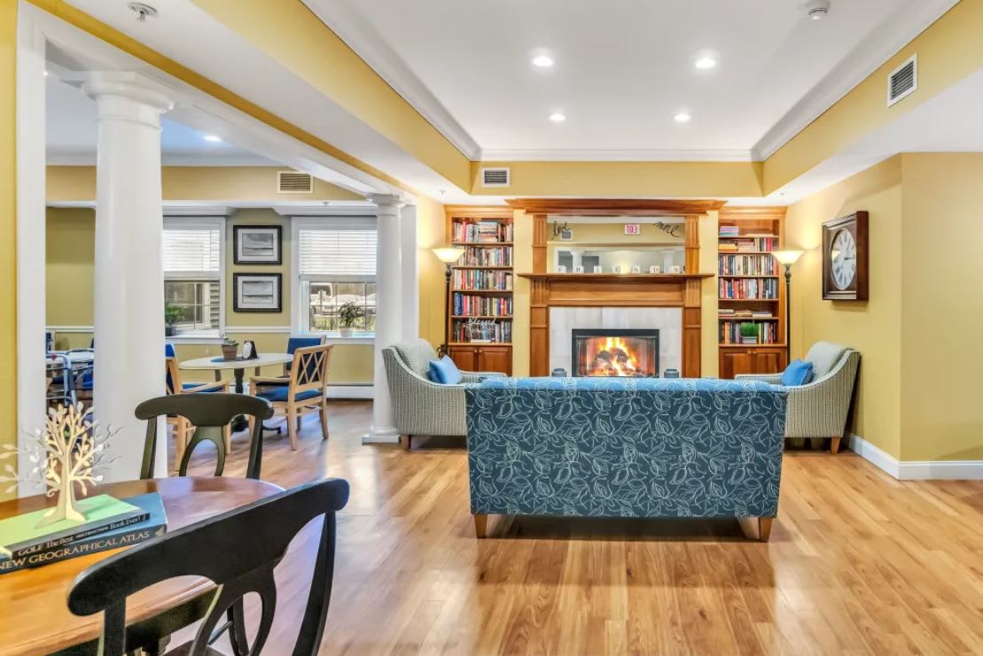 A cozy living room with a fireplace and bookshelves, featuring a blue couch and wooden floors.