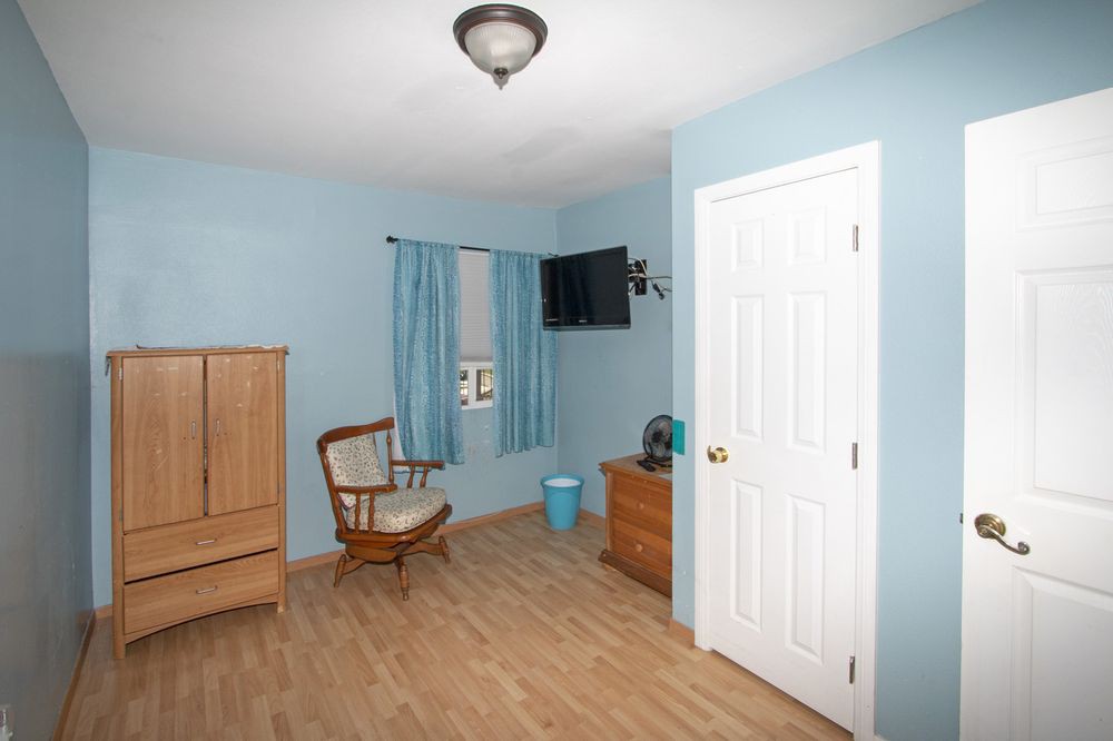 A cozy bedroom with blue walls features a rocking chair, wardrobe, television, and wooden flooring.