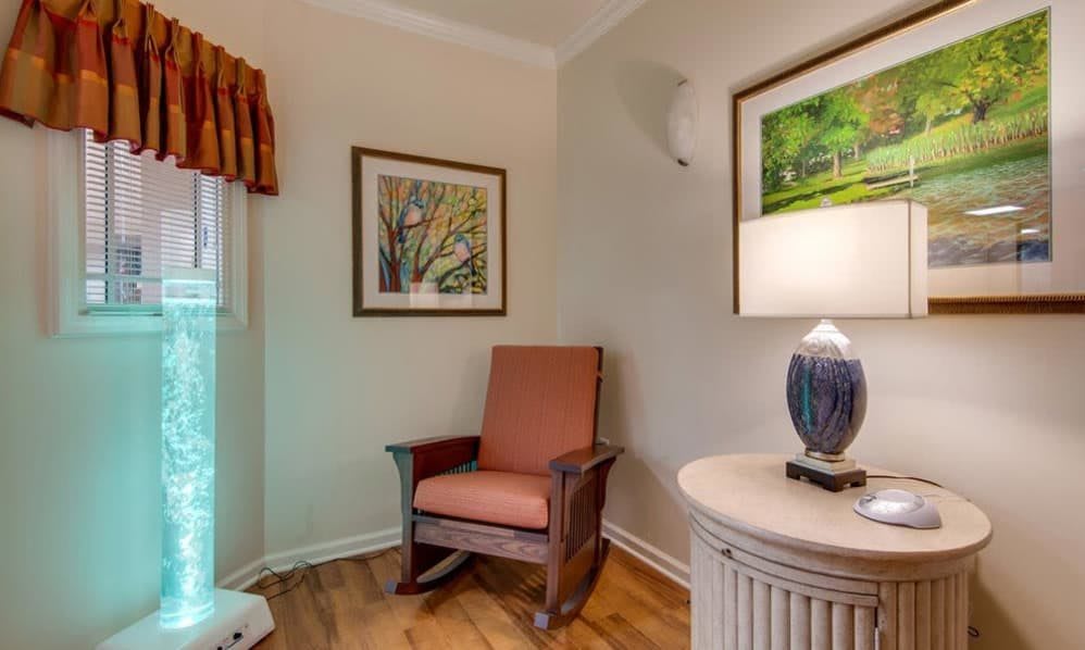Cozy corner with a wooden chair, lamp on a table, and framed art on the walls.