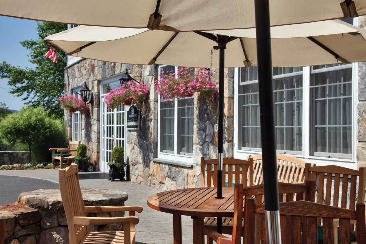 A cozy outdoor patio with wooden tables and chairs under large umbrellas, adorned with hanging flower baskets.